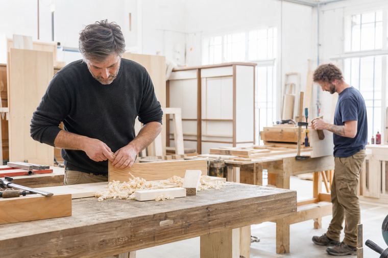 Artigiano in piedi accanto al proprio tavolo da lavoro in una falegnameria.